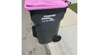 Dumpster Diverz employee in purple uniform checking residential trash cart in front of house